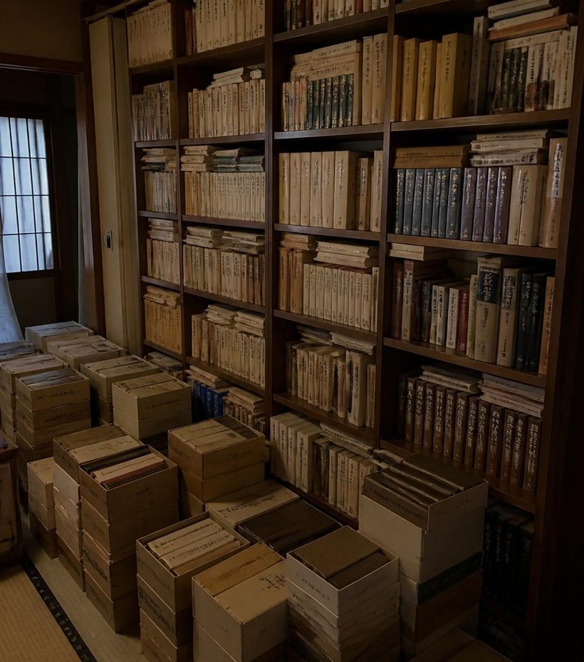 床から天井まで本が詰まった書棚と、足元に積み上げられた全集の箱